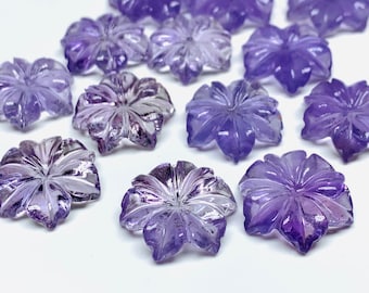 Könnte beinhalten: Eine Sammlung von 13 lila Amethyst-Cabochons in Blütenform. Die Cabochons sind facettiert und haben eine glatte, polierte Oberfläche.