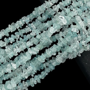 Puede incluir: Primer plano de hilos de virutas de piedras preciosas aguamarina, en un tono azul pálido. Las virutas tienen formas irregulares, creando una apariencia texturizada. Las cuentas están ensartadas, perfectas para la fabricación de joyas.