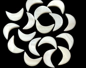 May include: A collection of 18 white mother of pearl crescent moon shaped charms. The charms are arranged in a circular pattern on a black background.