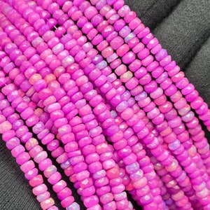 May include: A strand of pink opal beads with a faceted, barrel shape. The beads are strung on a clear thread and have a slight iridescent sheen.