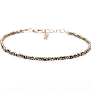 Puede incluir: Un delicado brazalete de oro con pequeñas cuentas redondas de pirita. El brazalete tiene un diseño simple y minimalista, perfecto para el uso diario.
