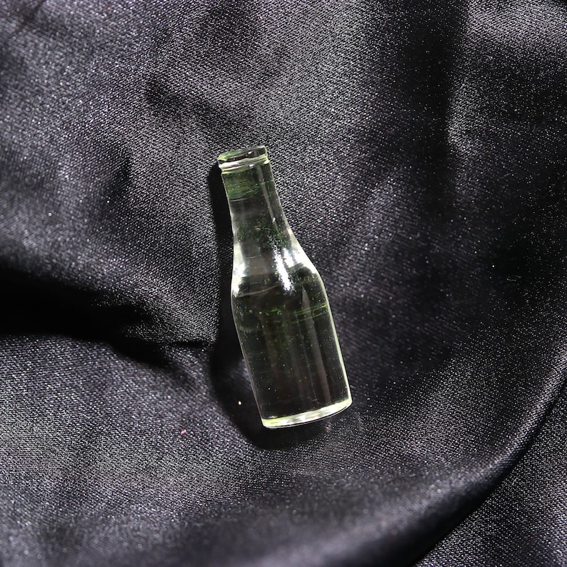Puede incluir: Una botella de vidrio transparente con una superficie texturizada. La botella est&aacute; vac&iacute;a y tiene un fondo redondeado.
