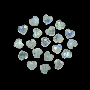 May include: A collection of heart-shaped moonstone gemstones. Each stone has a faceted surface, displaying a range of colors including white, blue, and iridescent flashes. The gemstones are arranged against a black background.