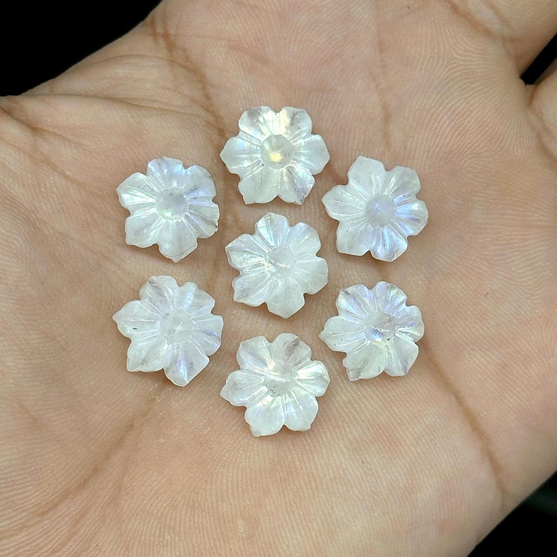 May include: Seven iridescent, carved flower-shaped gemstones. The gemstones are white with subtle blue and purple hues. The flowers have detailed petal carvings and are arranged in a circular pattern, ideal for jewelry making or crafts.