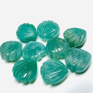May include: A collection of eight teal green gemstone beads carved in the shape of seashells. The beads are smooth and polished, with a slightly iridescent finish.