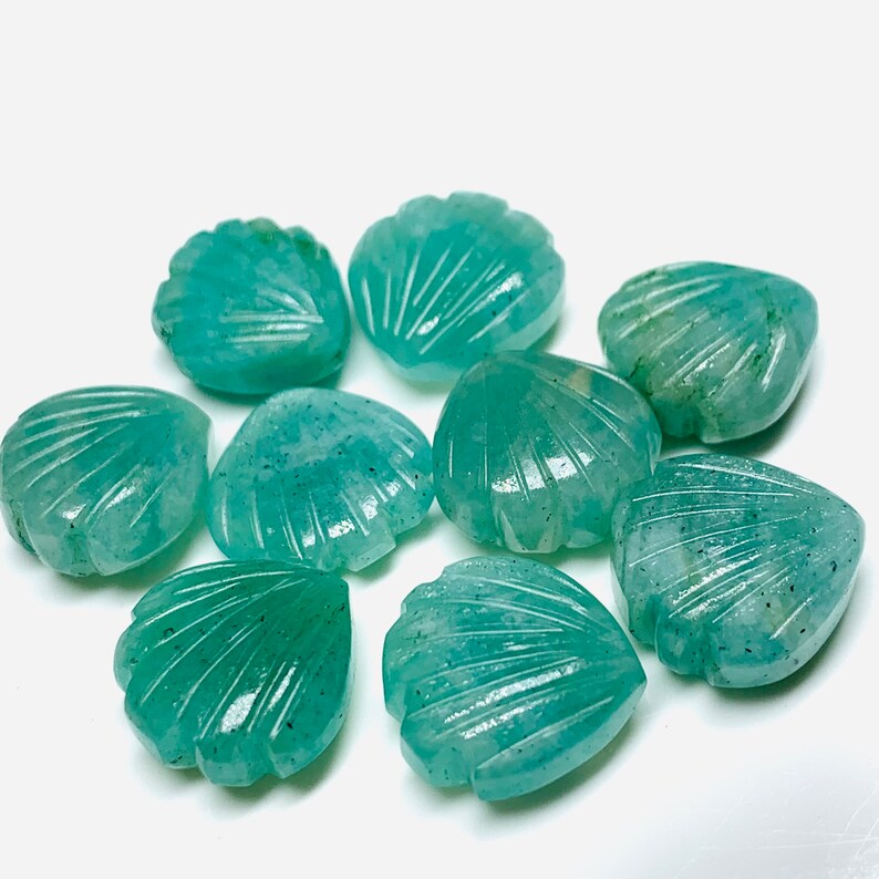 May include: A collection of eight teal green gemstone beads carved in the shape of seashells. The beads are smooth and polished, with a slightly iridescent finish.