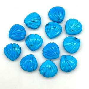 Könnte beinhalten: Zwölf türkisfarbene Edelsteinkabochons, die in Form einer Muschel geschnitzt sind. Die Cabochons haben eine leuchtende blaue Farbe und eine glatte, polierte Oberfläche.