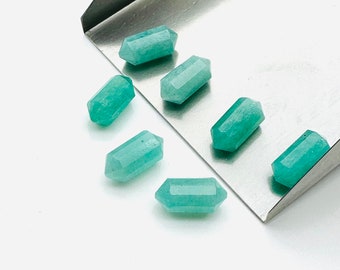 May include: Seven teal green gemstone points, each with a hexagonal shape, are arranged on a silver tray. The points are all roughly the same size and shape.