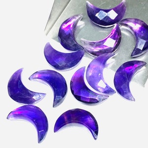 May include: A collection of ten crescent moon shaped amethyst gemstones. The gemstones are a deep purple color with a slight iridescent sheen.