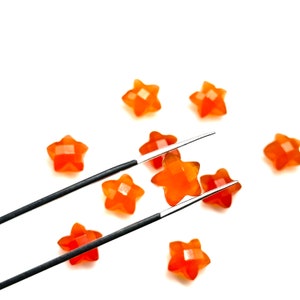 May include: A set of orange star-shaped candy pieces, one of which is being held by a pair of silver tweezers.