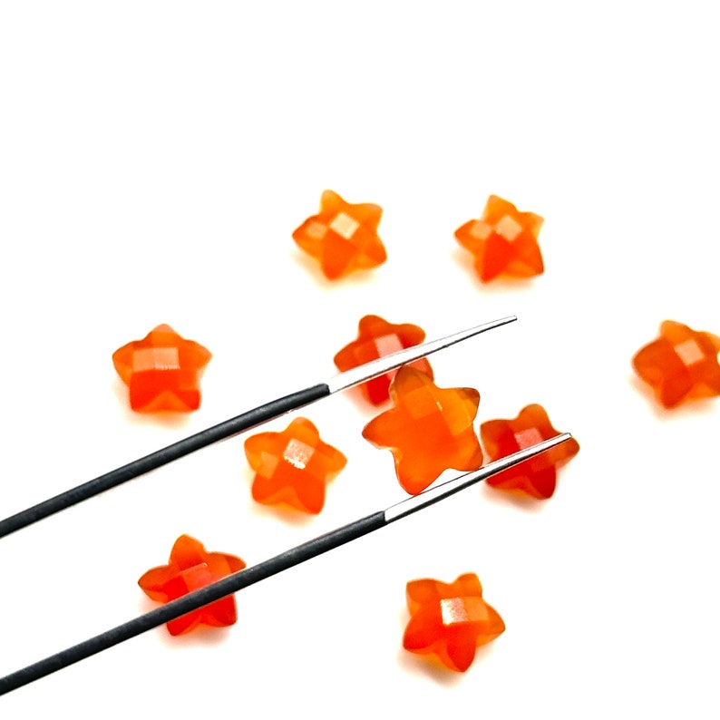 May include: A set of orange star-shaped candy pieces, one of which is being held by a pair of silver tweezers.