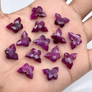 May include: A selection of magenta-coloured, butterfly-shaped gemstones. Each gemstone is multi-faceted, creating a sparkling effect. The butterfly shapes are consistent in size and design, with a faceted cut.
