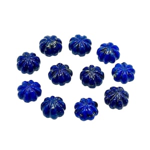 Peut inclure: Douze perles de pierres précieuses en lapis-lazuli bleu foncé. Chaque perle est sculptée avec un motif floral. Les perles sont dispersées sur un fond blanc, mettant en valeur leur couleur riche et leurs détails complexes.