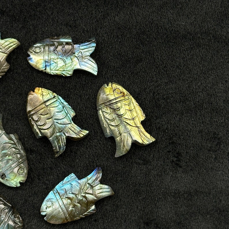 Puede incluir: Una colecci&oacute;n de esculturas de peces de labradorita iridiscente. Los peces est&aacute;n tallados en piedra de labradorita natural y tienen una variedad de colores, incluyendo azul, verde y dorado.