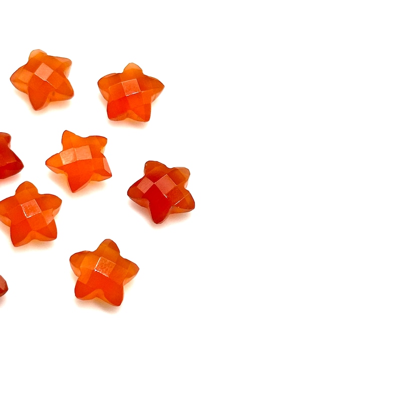 May include: A group of eight orange star-shaped gemstone beads. The beads are faceted and have a polished finish.