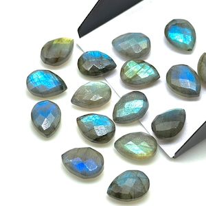Puede incluir: Una colección de 15 piedras preciosas de labradorita en forma de lágrima. Las piedras son una mezcla de gris, azul y verde con destellos iridiscentes.