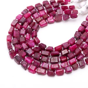 May include: Close-up of several strands of faceted, deep magenta-coloured gemstone beads. The beads are rectangular and strung together with white string. The background is white, highlighting the vibrant colour of the gemstones.