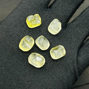 May include: Six translucent yellow faceted gemstones on a black fabric background.