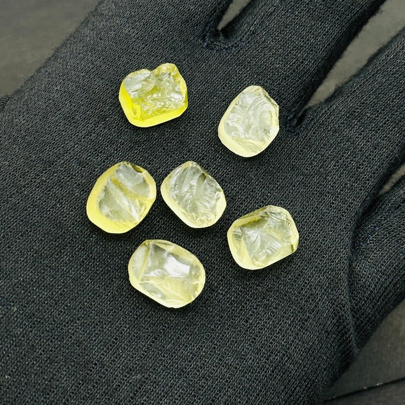 May include: Six translucent yellow faceted gemstones on a black fabric background.