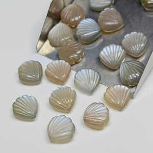 Könnte beinhalten: Eine Sammlung von irisierenden, geschnitzten Edelsteinschalen in Weiß- und Hellbrauntönen. Die Muscheln sind herzförmig und haben ein zartes, geschnitztes Design.