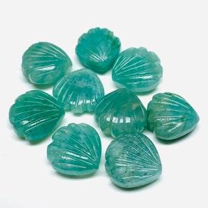 May include: A collection of eight teal green gemstone shell-shaped beads. The beads are carved with a detailed shell pattern and have a smooth, polished finish.