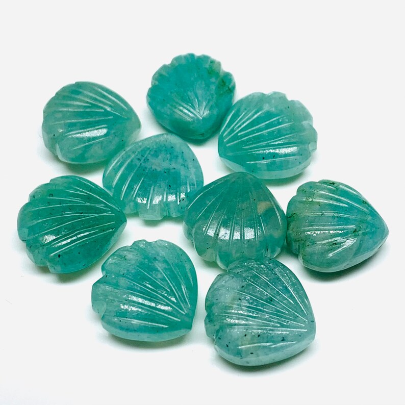 May include: A collection of eight teal green gemstone shell-shaped beads. The beads are carved with a detailed shell pattern and have a smooth, polished finish.
