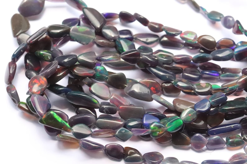 May include: A strand of dark iridescent opal beads, each bead is a unique, freeform shape with a smooth, polished finish.