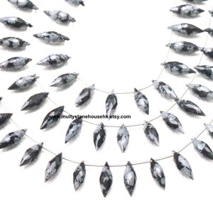 Könnte beinhalten: Eine Kette aus schwarzen und weißen Schneeflocken-Obsidianperlen, auf silbernem Draht gefädelt. Die Perlen sind facettiert und haben eine Tropfenform. Die Kette ist etwa 45 cm lang.