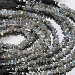 May include: Strands of iridescent labradorite gemstone beads. The beads are teardrop-shaped and gray with flashes of blue and green. Each strand is finished with a black tassel.