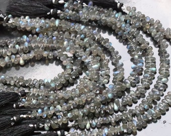 May include: Strands of iridescent labradorite gemstone beads. The beads are teardrop-shaped and gray with flashes of blue and green. Each strand is finished with a black tassel.