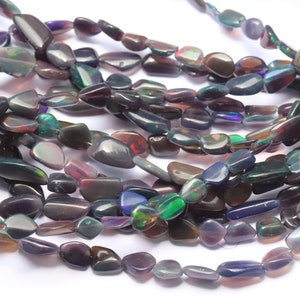 May include: A strand of iridescent black opal gemstone beads. The beads are irregularly shaped and have a smooth, polished finish. The beads are strung on a clear thread and are ready to be used for jewelry making.