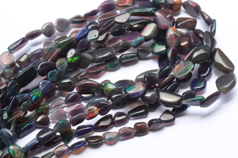 May include: A strand of dark, iridescent, teardrop-shaped opal beads. The beads have a black base with flashes of green, red, and purple.