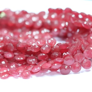 Pode incluir: Um fio de contas de pedras preciosas cor-de-rosa. As contas são facetadas e têm um formato ligeiramente irregular. As contas são enfiadas num fio transparente.