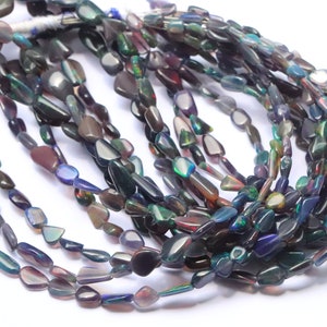May include: A strand of iridescent black opal gemstone beads. The beads are irregular in shape and have a variety of colors, including green, blue, purple, and red.
