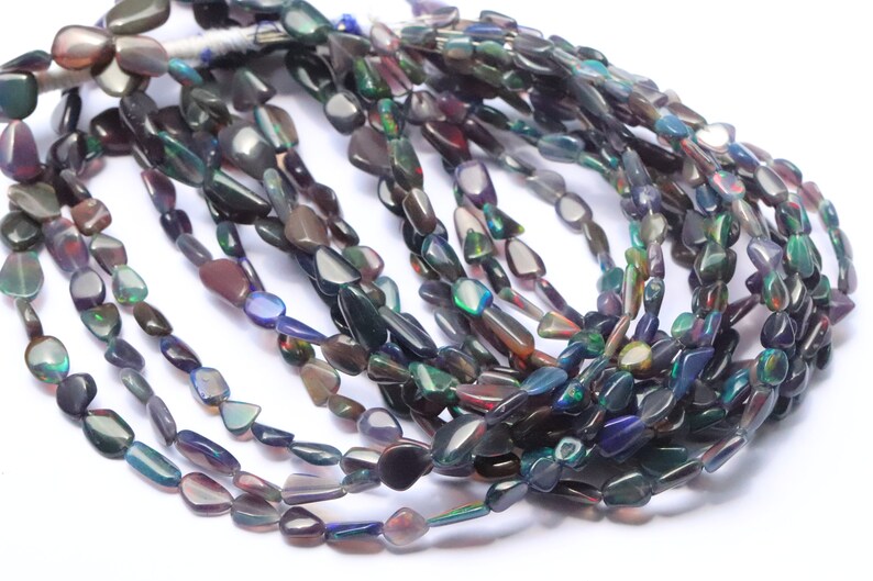 May include: A strand of iridescent black opal gemstone beads. The beads are irregular in shape and have a variety of colors, including green, blue, purple, and red.
