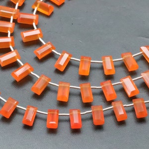 以下が含まれることがあります： オレンジのカーネリアン宝石ビーズのストランド。各ビーズは長方形でファセットカットされています。ビーズは銀線に糸で通されています。