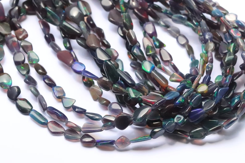 May include: A strand of iridescent black opal gemstone beads. The beads are teardrop shaped and have a smooth, polished finish.