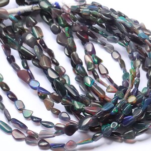 May include: A strand of dark iridescent opal gemstone beads in a teardrop shape. The beads are strung on a clear thread and are approximately 10mm in length.
