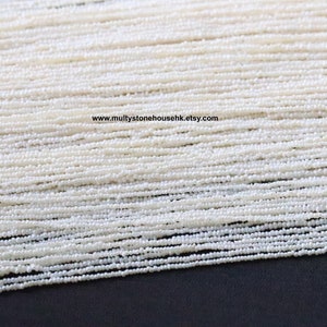 Op de afbeelding: Een close-up van een streng witte parels. De parels zijn klein en rond en zijn aan elkaar geregen op een dun draad. De parels zijn in een nette, gelijkmatige rij gerangschikt en ze zijn allemaal even groot en even gevormd.