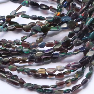 May include: A strand of dark iridescent gemstone beads, with a mix of green, blue, and purple hues. The beads are irregularly shaped and have a smooth, polished finish.