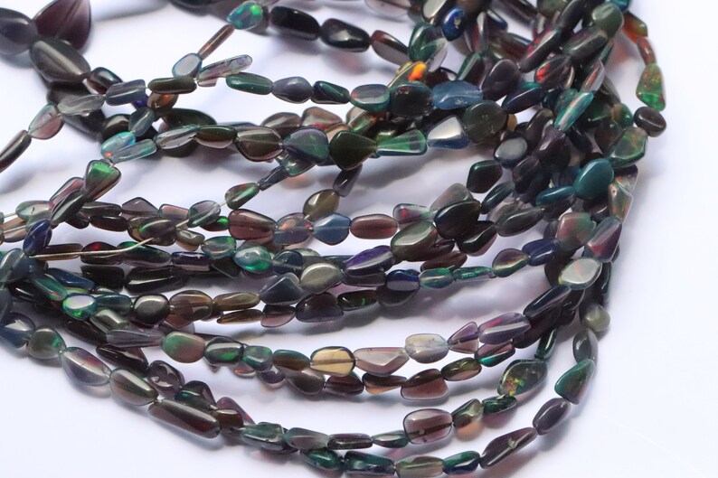 May include: A strand of dark iridescent gemstone beads, with a mix of green, blue, and purple hues. The beads are irregularly shaped and have a smooth, polished finish.