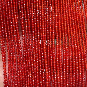 May include: Strands of faceted, reddish-orange gemstone beads. The beads are small and strung together, creating a textured, shimmering effect. The beads are likely used for jewelry making, such as necklaces or bracelets.
