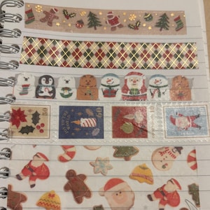 Puede incluir: Una variedad de cintas washi decorativas con temática navideña. Los diseños incluyen hombres de jengibre, Papá Noel, árboles de Navidad y patrones festivos. Las cintas están dispuestas en una página de cuaderno espiral.