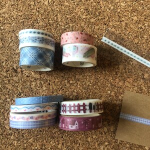 Puede incluir: Surtido de cintas washi decorativas con varios patrones, incluyendo diseños florales, geométricos y de casas. Las cintas son en tonos de azul, rosa y blanco.