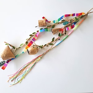 Op de afbeelding: Een handgemaakte windgong met drie kleine kurken bellen, versierd met kleurrijke linten, kunstgroen en een veer. De windgong heeft een ophanglus en een kwast van veelkleurige draden.