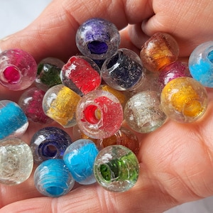 Puede incluir: Una colección de cuentas de vidrio de colores con varios patrones y texturas. Las cuentas son redondas y tienen un agujero en el centro, lo que sugiere que son para hacer joyas o manualidades.