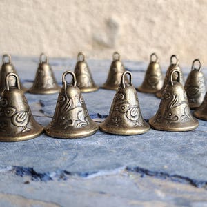 Könnte beinhalten: Eine Sammlung von 12 kleinen, antiken, goldfarbenen Glocken mit aufwendigen Designs. Jede Glocke hat ein einzigartiges Muster mit einem Vogel- oder Tiermotiv.