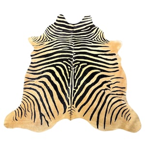 May include: A natural hide rug featuring a tan base colour with bold, black, symmetrical tiger-like stripes radiating from a central spine. The rug has an irregular, organic shape with curved edges, mimicking the natural silhouette of an animal hide.