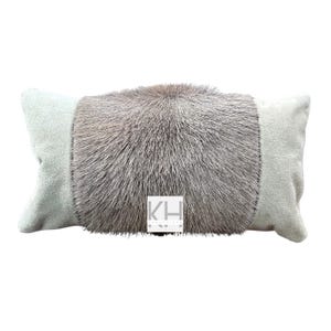 May include: Rectangular decorative pillow with a central section of gray fur and light gray suede-like fabric on the ends. The pillow has a soft, plush appearance. The pillow has a label with the letters "KH" on it.