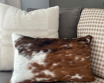 May include: A brown and white cowhide throw pillow with a white and brown checkered pattern background.